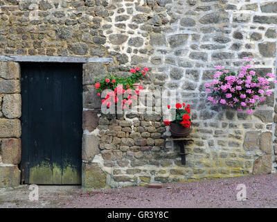 Schwarzen Holztür von einer rustikalen Scheune im Ortsteil La Gouaudiere, Normandie, Frankreich mit fröhlichen hängenden Blumenkörben. Stockfoto