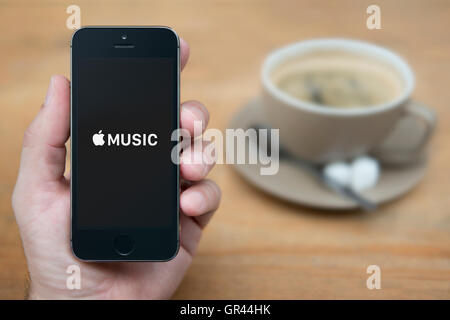 Ein Mann schaut auf seinem iPhone das Apple Music-Logo anzeigt, während setzte sich mit einer Tasse Kaffee (nur zur redaktionellen Verwendung). Stockfoto