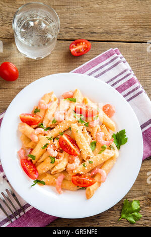 Penne-Nudeln mit Shrimps, Tomatensauce, Petersilie und geriebenen Parmesan über rustikale Holz Hintergrund Stockfoto