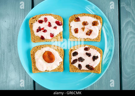 Brot mit Erdbeer-Sahne-Käse und Trockenfrüchte auf blaue Platte, gesundes Frühstück Einstellung von oben. Stockfoto