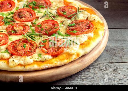 Pizza Margherita mit Tomaten, Käse, Basilikum und Rosmarin über rustikalen hölzernen Hintergrund hautnah Stockfoto