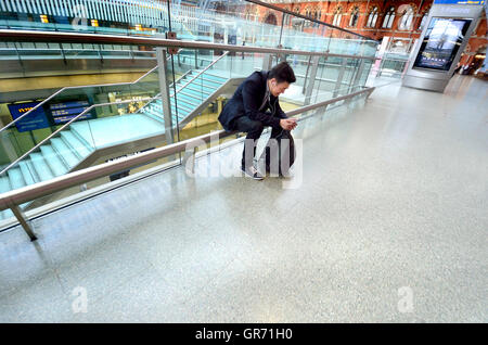 London, England, Vereinigtes Königreich. St Pancras Station - asiatischer Mann hören mit Kopfhörern auf seinem Handy Stockfoto