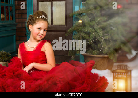 Kleines Winter begrüßt Prinzessin in eine kostbare Krone im roten Kleid Weihnachten und Neujahr in zauberhaften Urlaub Innenraum Stockfoto