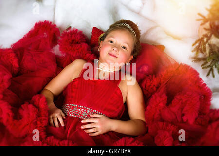 Kleines Winter Prinzessin in eine kostbare Krone im roten Kleid liegt auf Kunstschnee. Begrüßt, Weihnachten und Neujahr Stockfoto