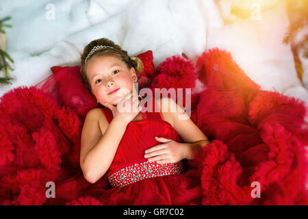Kleines Winter Prinzessin in eine kostbare Krone im roten Kleid liegt auf Kunstschnee. Begrüßt, Weihnachten und Neujahr Stockfoto
