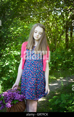 Schöne Teenager-Mädchen Wandern in Wäldern mit einem Korb voller Blumen mit Augen niedergeschlagen Stockfoto