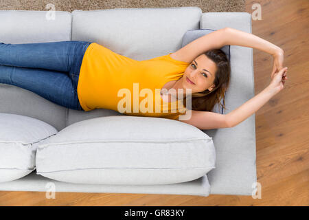 Blick von oben auf eine schöne und glückliche junge Frau liegt auf einem Sofa Stockfoto