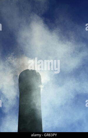 Rauch strömt aus einem Schornstein unter einem pulsierenden klaren blauen Himmel. CO2-Emissionen stehen ganz oben auf aktuelle Themen Bezug auf den Klimawandel Stockfoto