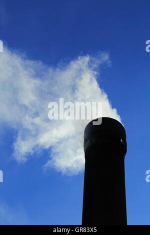 Rauch strömt aus einem Schornstein unter einem pulsierenden klaren blauen Himmel. CO2-Emissionen stehen ganz oben auf aktuelle Themen Bezug auf den Klimawandel Stockfoto