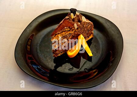 Schokoladen-Kuchen mit Mandeln und Pflaumen auf schwarzem Teller Stockfoto