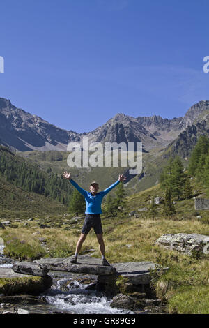 Wanderer In Siegerpose auf einer kleinen Brücke im Ötztal Stockfoto