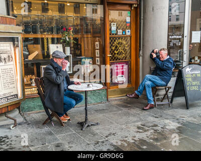Ein Erwachsene männliche Model seine Tasse Kaffee und einem Fotografen fotografieren sein Porträt vor einer Kaffee-Bar. Farb-Version. Stockfoto