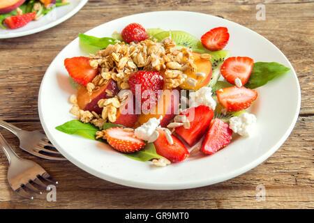 Frischer Obstsalat mit Müsli, Feta-Käse und Honig auf weißen Teller für gesundes Frühstück Stockfoto