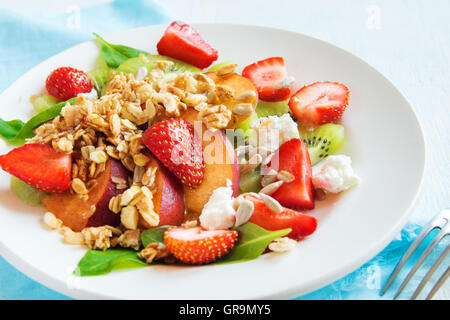 Frischer Obstsalat mit Müsli, Feta-Käse und Honig auf weißen Teller für gesundes Frühstück Stockfoto