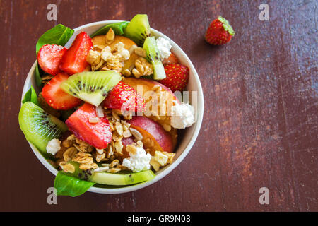 Frischer Obstsalat mit Müsli, Feta-Käse und Honig in Schale für gesundes Frühstück Stockfoto