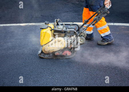 Worker nutzen Vibrations Platte Verdichter komprimiert Asphalt bei Straßenreparatur Stockfoto