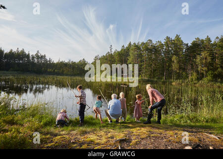 Großeltern und Enkelkinder Angeln am sonnigen Seeufer in Wäldern Stockfoto