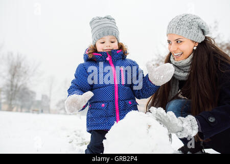 Mutter und Tochter im Winter Natur Schneemann bauen Stockfoto