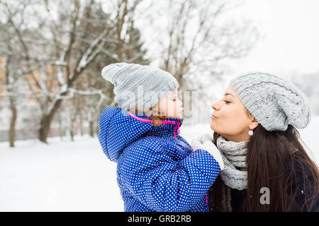 Mutter mit ihrer Tochter küssen außerhalb im Winter Natur Stockfoto