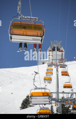 Sesselbahn mit Orangen Wetterschutzhauben, Beine mit Skiern, blauer Himmel Stockfoto