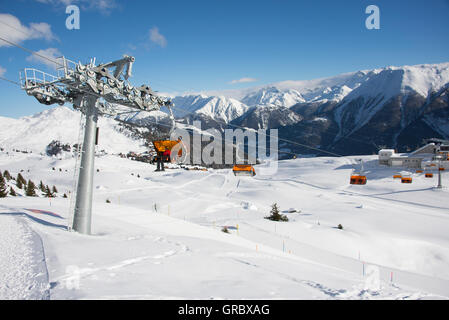 Sesselbahn mit Orangen Wetterschutzhauben an einem sonnigen Wintertag, blauer Himmel und Schnee bedeckte Berge im Hintergrund Stockfoto