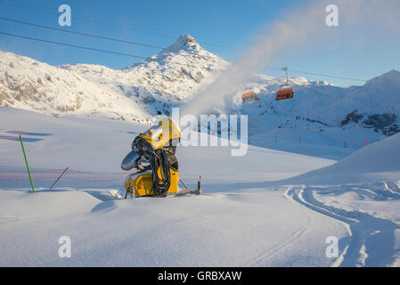 Schneefeld mit aktiven gelben Schneekanone, im Hintergrund Bettmerhorn und blauer Himmel Stockfoto