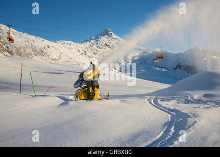 Schneefeld mit aktiven gelben Schneekanone, im Hintergrund Bettmerhorn und blauer Himmel Stockfoto