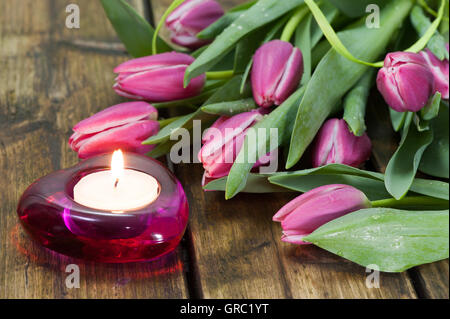 Tulpen, liegend auf einem alten hölzernen brennt Tisch neben eine Kerze Stockfoto