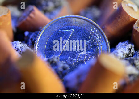 Volle Aschenbecher mit Zigarettenkippen und Euro-Münze Stockfoto