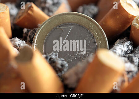 Volle Aschenbecher mit Zigarettenkippen und Euro-Münze Stockfoto