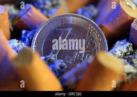 Volle Aschenbecher mit Zigarettenkippen und Euro-Münze Stockfoto