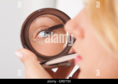 Junge Blondine In Mascaras In der Kosmetikspiegel Stockfoto