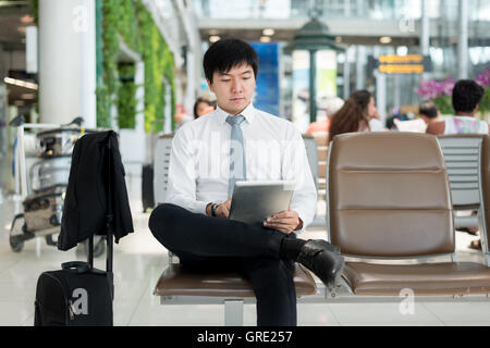 Asiatische Geschäftsmann mit digital-Tablette während der Wartezeit in der Lounge am Flughafen. Business Travel-Konzept. Stockfoto