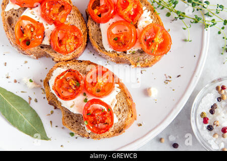 Leckere Bruschetta mit gerösteten Tomaten, Feta-Käse und Kräutern auf weißen Teller Stockfoto