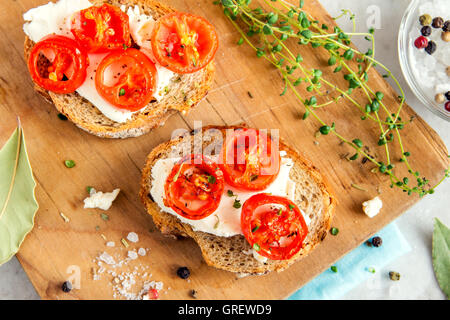 Leckere Bruschetta mit gerösteten Tomaten, Feta-Käse und Kräutern auf Holzbrett Stockfoto