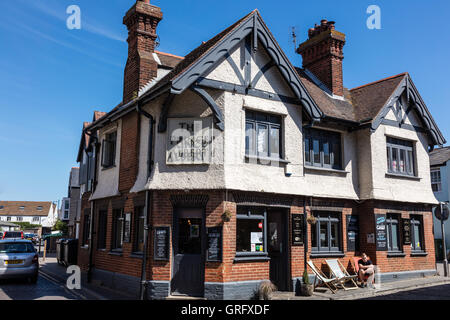 Ein Mann sitzt in einem Liegestuhl außerhalb der Prinz Albert eine Kneipe im Hafen Straße, Whitstable, Kent, UK Stockfoto