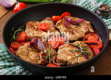 Saftiges Schweinesteak mit Rosmarin und Tomaten auf Pfanne Stockfoto