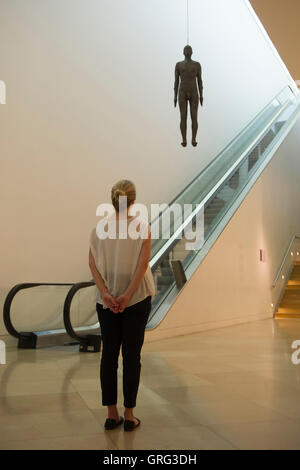 Eine Frau sieht eine lebensgroße Skulptur von Antony Gormley - Objekt, 1999 - die von der Decke auf den Ondaatje Wing Main Hall von der National Portrait Gallery, London aufgehängt ist. Stockfoto