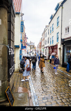 Gruppe der orientalischen Touristen und verschiedene andere Leute auf der Church Street, auf einer sehr regnerischen Tag. in Whitby Stockfoto