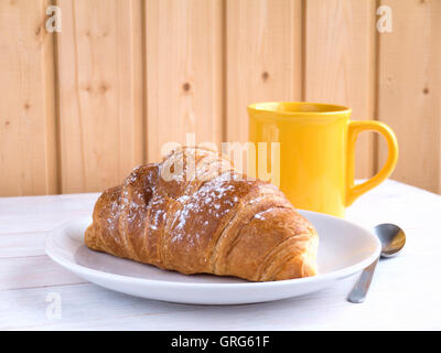 Kontinentales Frühstück Croissant und Kaffee in der gelben Tasse auf dem weißen Holztisch Stockfoto