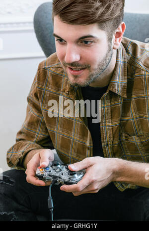 Ein jungen dunkelhaarigen Mann lehnt sich nach vorne auf seinem Stuhl halten Sie einen Gamecontroller. Stockfoto