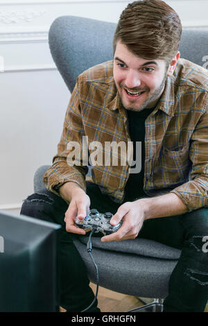 Ein jungen dunkelhaarigen Mann lehnt sich nach vorne auf seinem Stuhl halten Sie einen Gamecontroller. Stockfoto