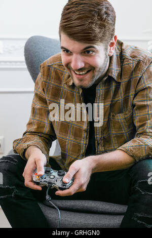 Ein jungen dunkelhaarigen Mann lehnt sich nach vorne auf seinem Stuhl halten Sie einen Gamecontroller. Stockfoto