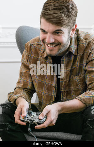 Ein jungen dunkelhaarigen Mann lehnt sich nach vorne auf seinem Stuhl halten Sie einen Gamecontroller. Stockfoto