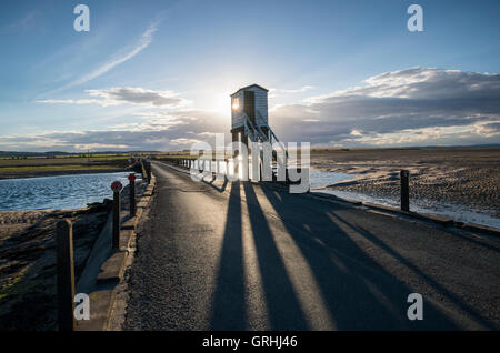 Hinterleuchtete niedrige Sonne wirft Schatten aus dem Notruf-Uhr-Turm auf dem Damm auf der Heiligen Insel, Northumberland England UK Stockfoto