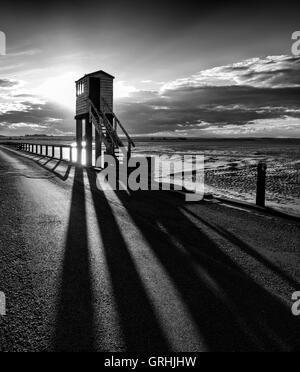 Hinterleuchtete niedrige Sonne wirft Schatten aus dem Notruf-Uhr-Turm auf dem Damm auf der Heiligen Insel, Northumberland England UK Stockfoto