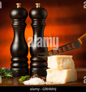 Stücke von Parmesan-Käse auf einem Holzbrett wird geschnitten mit Käsemesser mit Gewürzen auf einem hölzernen Restauranttisch in Stockfoto