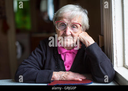 Ältere Frau in Gläser am Tisch sitzen. Stockfoto