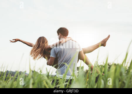 Sicht nach hinten gedreht der Mann trägt Frau im ländlichen Bereich. Paar genießt draußen auf der Wiese. Stockfoto