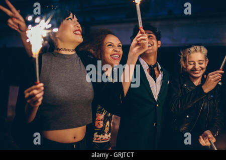 Junge Freunde halten Wunderkerzen heraus auf der Straße in der Nacht. Gruppe von Mann und Frau mit Nacht Party mit Wunderkerzen. Stockfoto